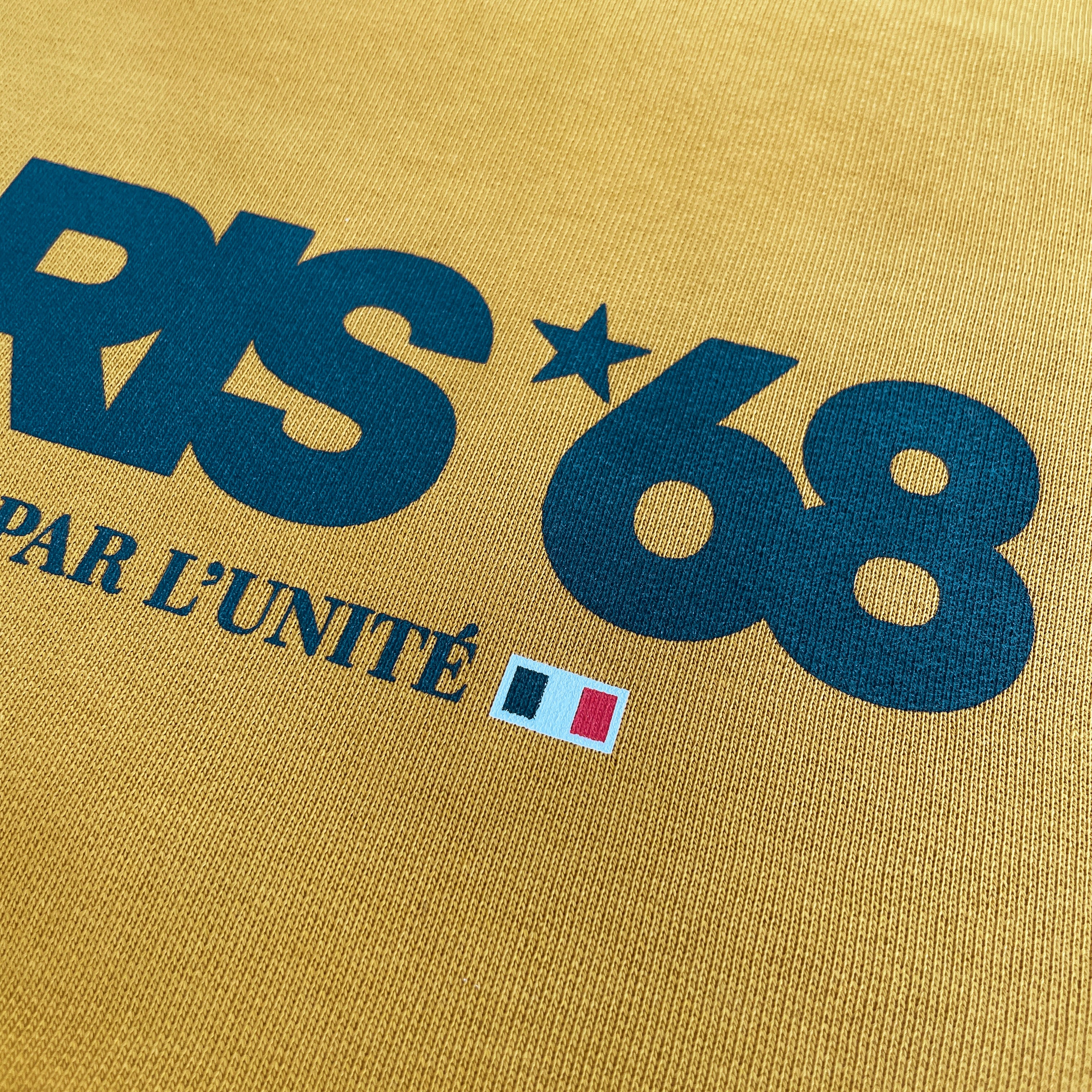 Close-up of a yellow fabric with blue text and a flag emblem.