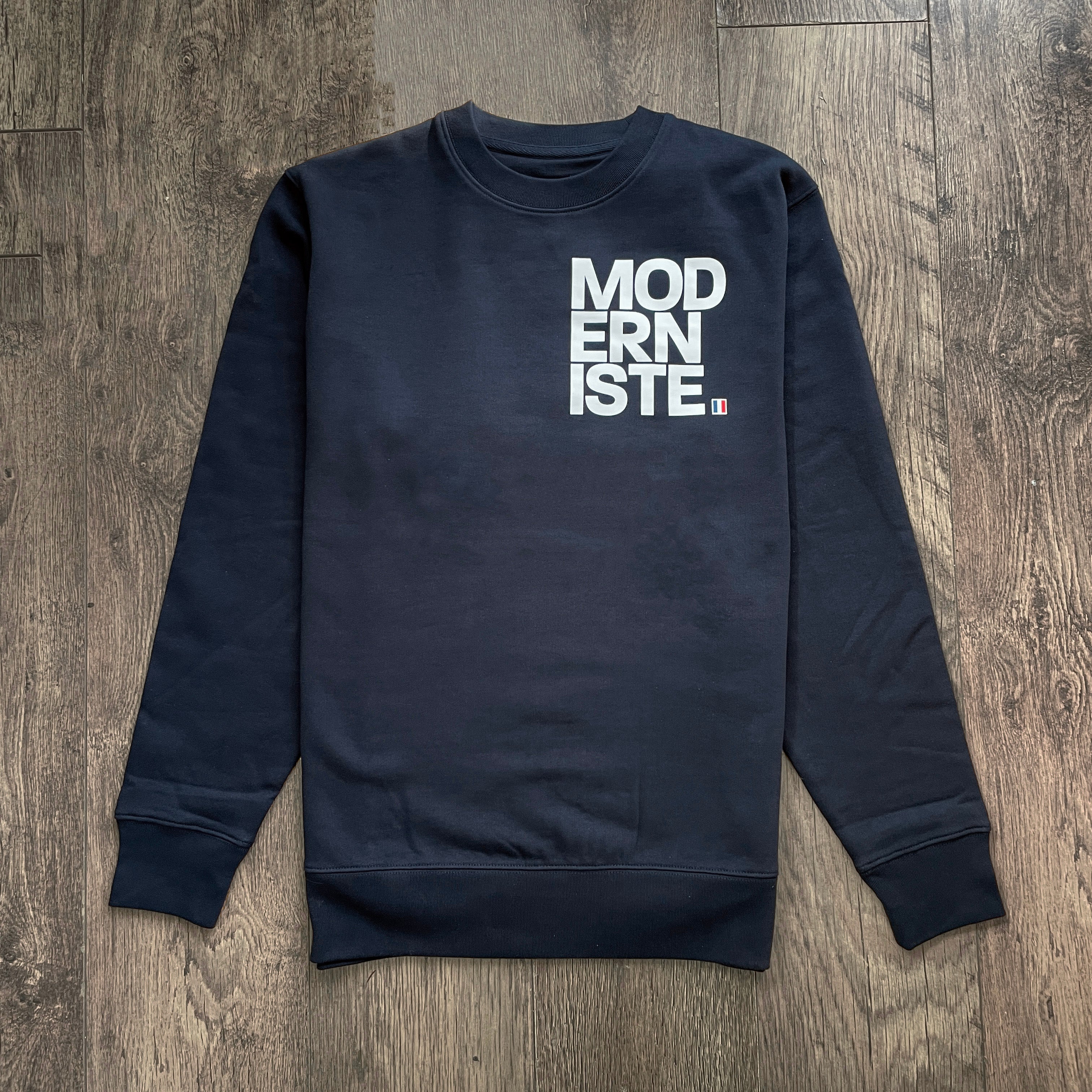 Navy blue sweatshirt with 'MODERNISTE' text on a wooden surface