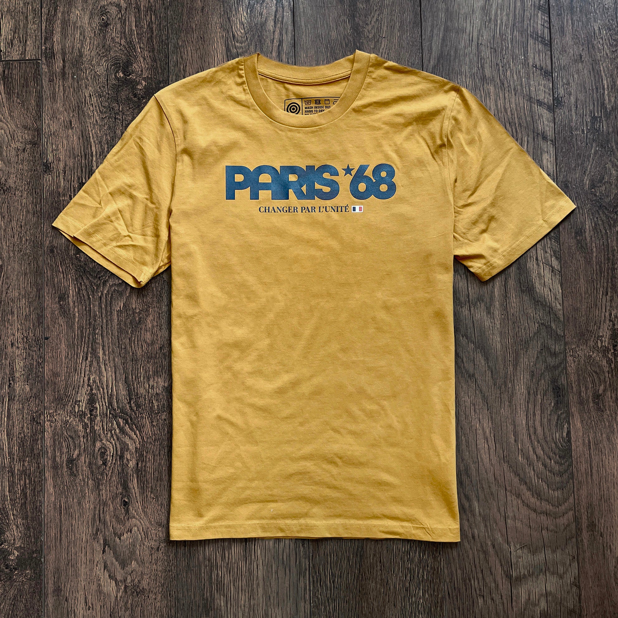 Yellow t-shirt with 'PARIS *68' text on a wooden surface